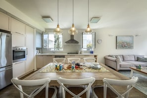 A modern kitchen with white cabinetry, a dining table with chairs, and pendant lights. - Stunning 2BR Apartment in Beeri (Tel Aviv)