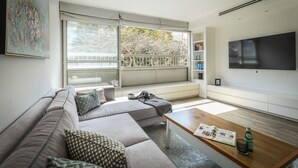 Ein modernes Wohnzimmer mit einem Ecksofa, einem Couchtisch und einem großen Fenster mit Blick auf Bäume.