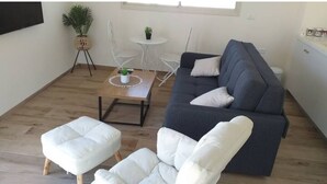Ein modernes Wohnzimmer mit einem dunkelgrauen Sofa, einem weißen Pouf und einem kleinen runden Tisch mit einer Pflanze.