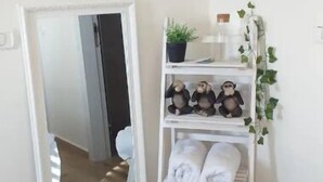 Ein Zimmer mit einem großen Spiegel, einem weißen Regal mit Handtüchern, einer kleinen Pflanze und einem Spiegel, der das Zimmer reflektiert.