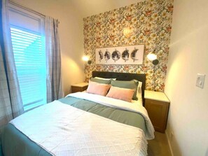 A neatly made bed with a floral wallpaper and a moon phase artwork above it.