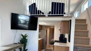 Cocina compacta con comedor, televisor montado en la pared y una escalera que sube a un nivel superior.