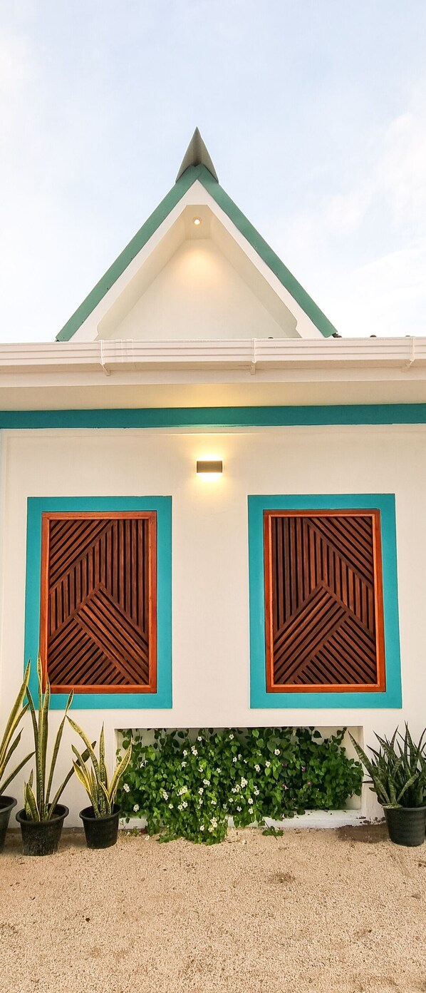 A building with a white facade, green roof, and two wooden decorative panels with geometric patterns.