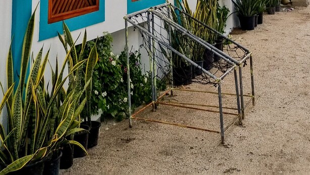 Een gebouw met een witte gevel en turquoise accenten, met grote houten deuren en een metalen trap die naar een overdekt gebied leidt.