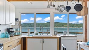 A kitchen with white cabinets, a wooden countertop, and a view of a lake and mountains. - Keys on the Canal - Stunning Beachfront Bungalow! (Belfair)