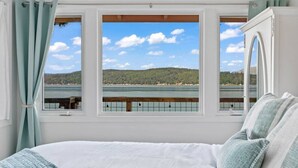 A bedroom with a large bed, a view of a lake, and a wooden deck. - Keys on the Canal - Stunning Beachfront Bungalow! (Belfair)