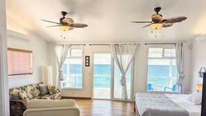 Een slaapkamer met een bed, een bank, een stoel en uitzicht op de zee door grote ramen.