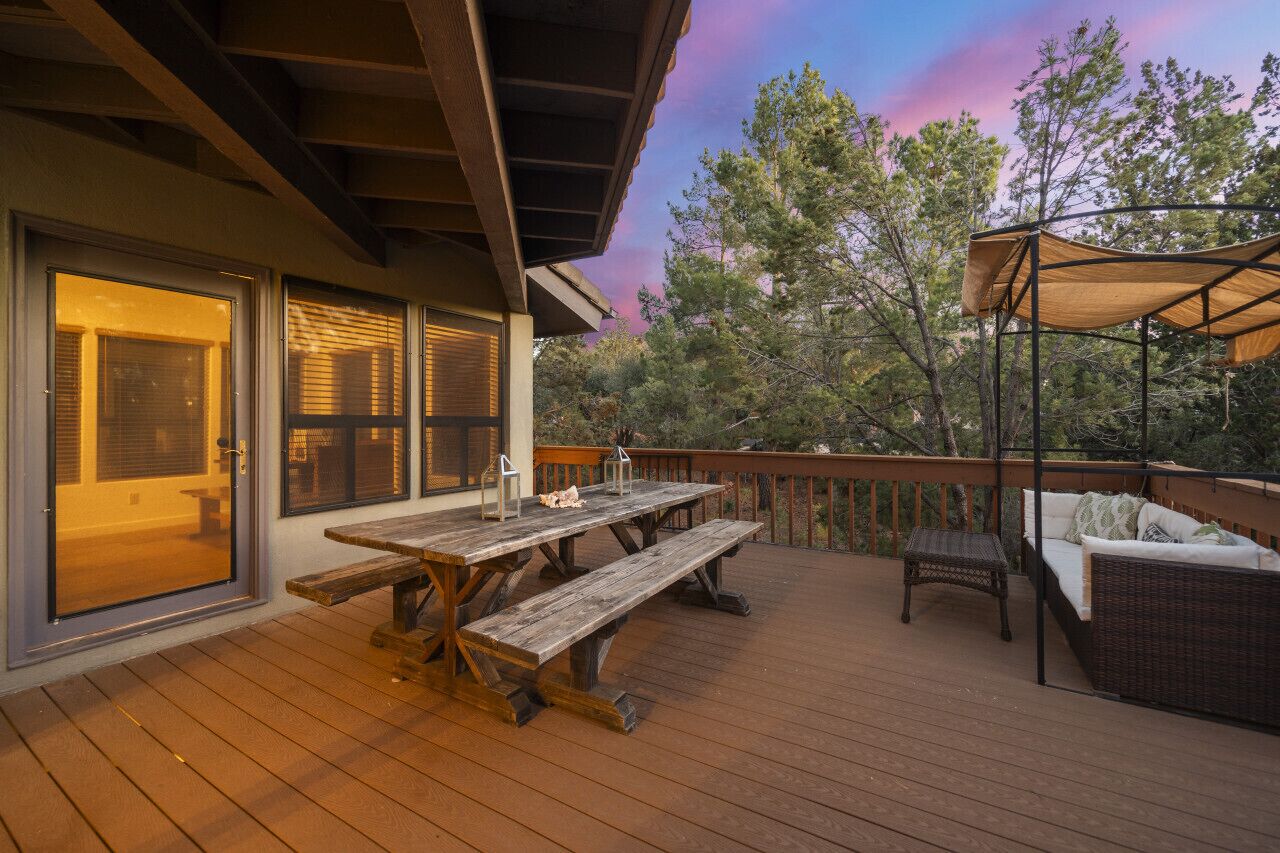 Une terrasse en bois avec une table de pique-nique et des sièges d’extérieur, donnant sur une zone boisée.