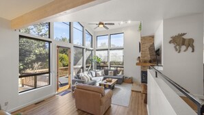 Un salon spacieux avec un grand canapé, une table basse et une cheminée. De grandes fenêtres laissent entrer la lumière naturelle et offrent une vue sur l’extérieur.