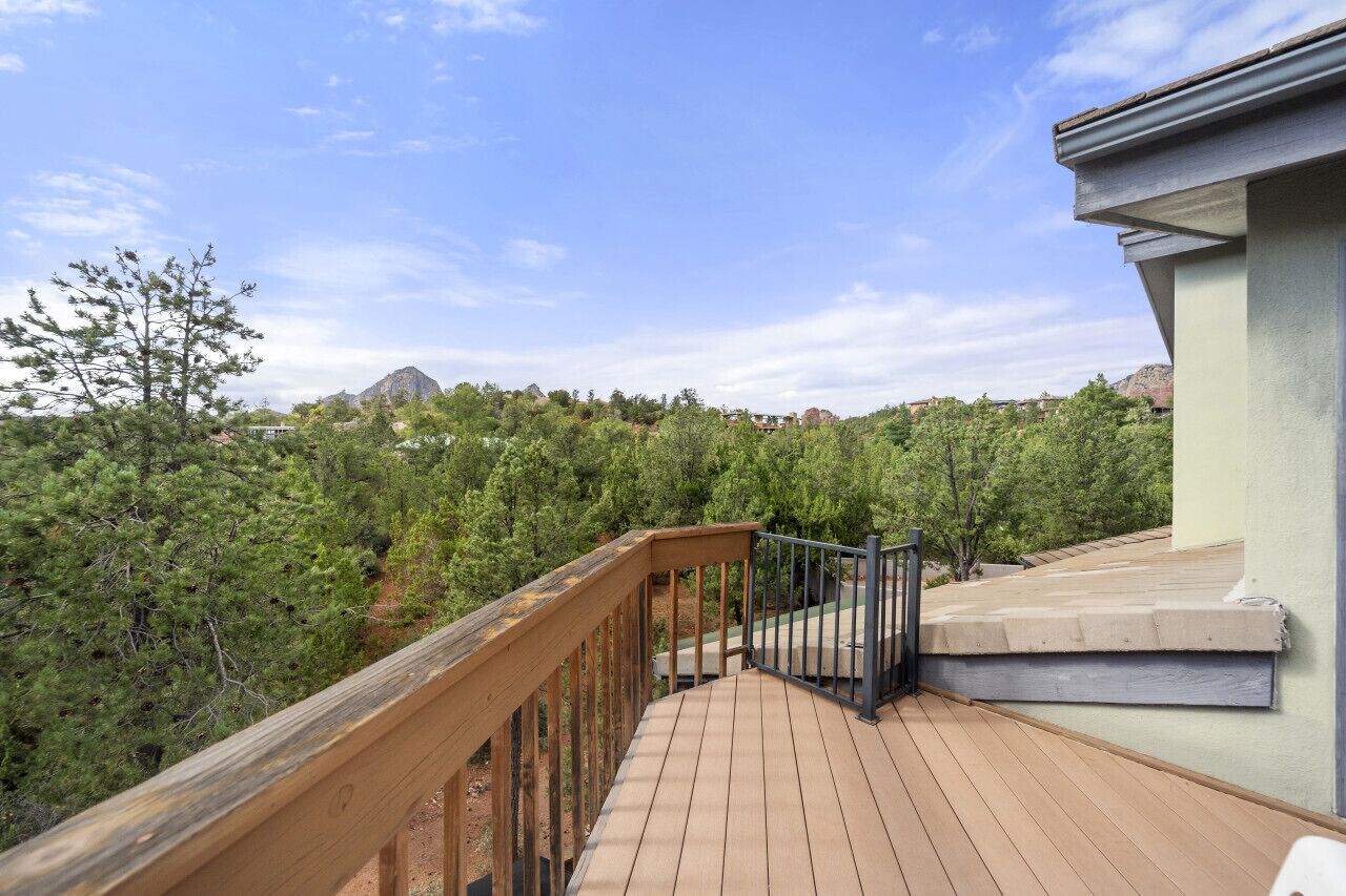 Um deck de madeira com guarda-corpo de metal, com vista para uma área arborizada e montanhas distantes.