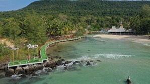 A coastal area with a bridge leading to a beach, surrounded by lush greenery and a mountain in the background. - Bird Nest Villas by Mafiya (Koh Rong)