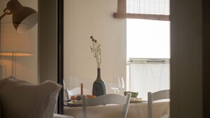 Un comedor con una mesa dispuesta para dos personas, un florero con flores secas y una ventana con cortinas.