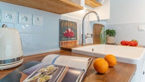 Una cocina con un hervidor blanco, un libro de cocina y dos naranjas sobre la encimera.