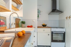 A kitchen with white cabinets, a stainless steel sink, a stove, and a countertop with oranges and tomatoes. - Bel Appartement Lumineux à Biarritz (Biarritz)