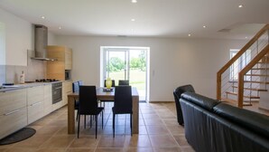 A modern kitchen with a dining area, a sofa, and a staircase.