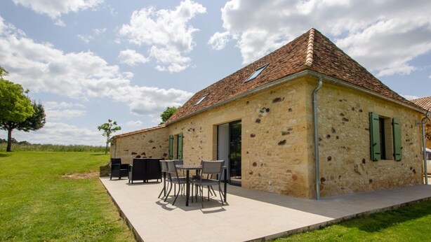 A stone building with a tiled roof, outdoor seating, and a grassy area.