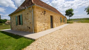 A stone building with a tiled roof, a gravel driveway, and a grassy area.