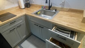 Moderni keittiö, jossa on harmaat kaapit, puinen työtaso, mustalla hanalla varustettu pesuallas ja kahvinkeitin.