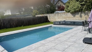A rectangular swimming pool with a tiled deck, surrounded by a stone wall and a grassy area.