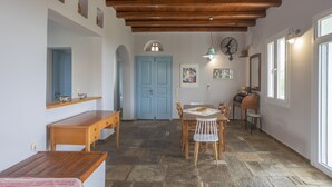 A dining area with a wooden table and chairs, a blue door, and a stone floor. - Cycladic Blue Andros (Γαύριο)