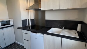 Kompakti keittiö, jossa on mikroaaltouuni, astianpesukone ja mustalla tasolla varustettu pesuallas.