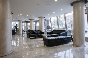 Un hall d’entrée doté d’un sol en marbre, de grandes colonnes et de mobilier moderne, notamment des canapés et une table basse.