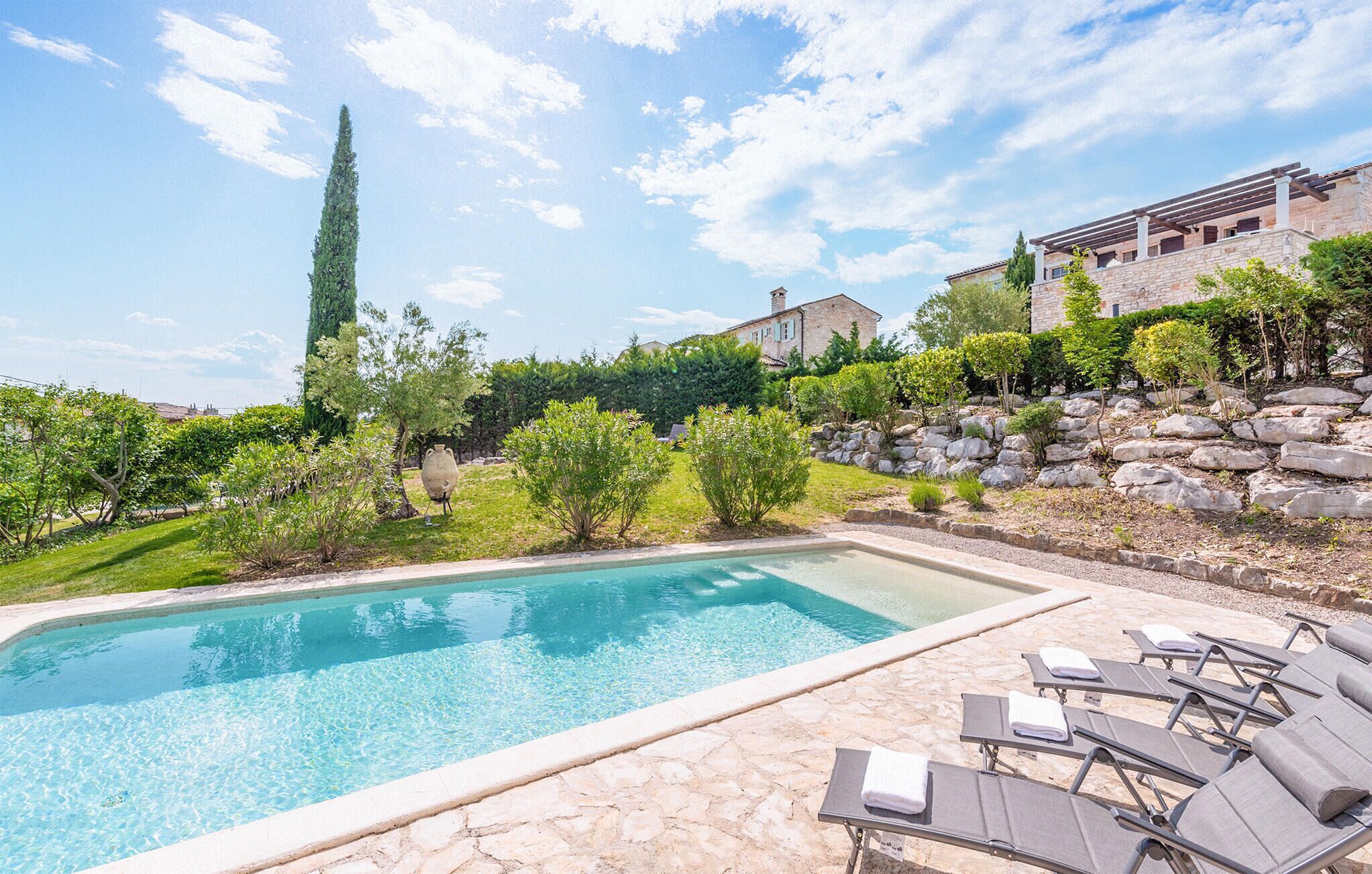 A swimming pool with lounge chairs, surrounded by a garden with various plants and a stone wall.