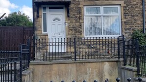 Una casa de dos pisos con fachada de piedra, una puerta blanca y una cerca de metal negro al frente.