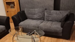 Una sala de estar con un sofá gris, una mesa de centro de vidrio y un mueble de madera con estantes.