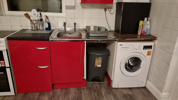 Una cocina compacta con lavadora, un lavamanos y un cubo de basura.