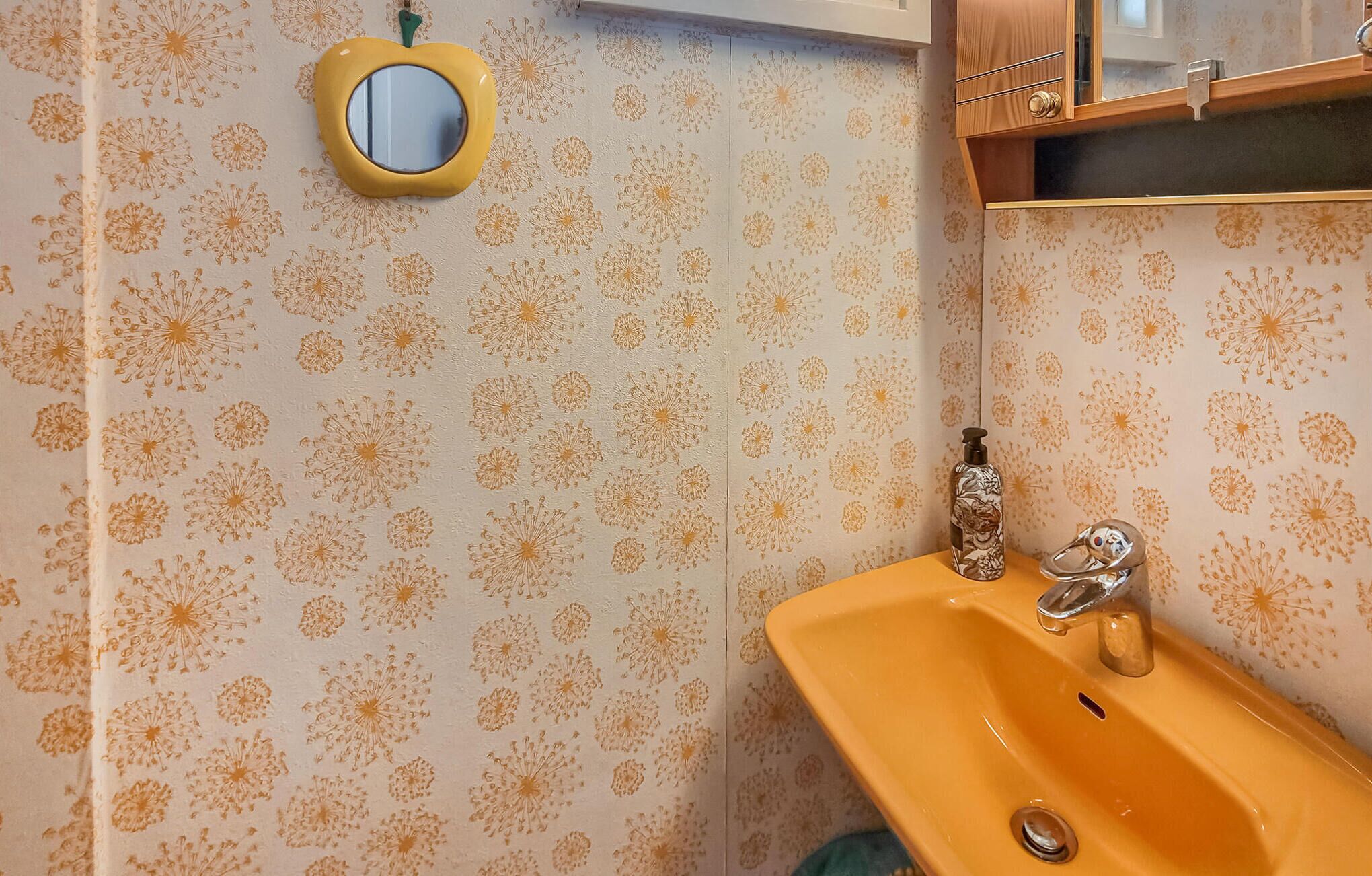 Une salle de bain avec un lavabo jaune, un miroir et un papier peint à motifs.