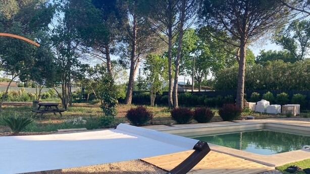 Un área junto a la piscina con un deck de madera, una silla de descanso blanca y una piscina.