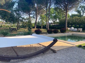 Un espace aménagé au bord de la piscine, avec une terrasse en bois, un fauteuil de relaxation blanc et une piscine.
