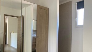 Una habitación moderna con armario correderas, un ventanal pequeño y una cocina a la vista.