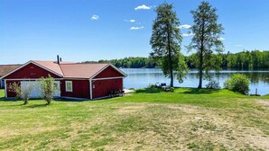 A red barn with a covered porch, a grassy yard, and a lake in the background. - Stunning home in Tingsryd with WiFi (Tingsryd)