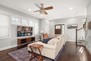 Un salon avec un canapé beige, une table basse, un téléviseur et un ventilateur de plafond.