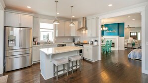 Een moderne keuken met roestvrijstalen apparatuur, een centraal eiland met barkrukken, en een heldere turquoise accentmuur.