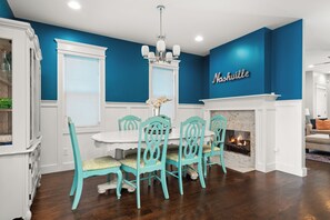 Un coin repas avec une table blanche et des chaises turquoise, une cheminée et un mur sur lequel est inscrit le mot « Nashville ».