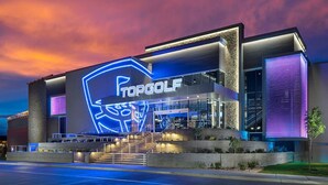 Ein modernes Gebäude mit einem großen, beleuchteten Logo und dem Schriftzug "TOPGOLF" an der Fassade.