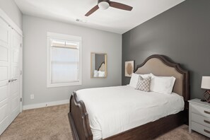 Une chambre à coucher avec un lit, une table de chevet, un miroir et un ventilateur de plafond.