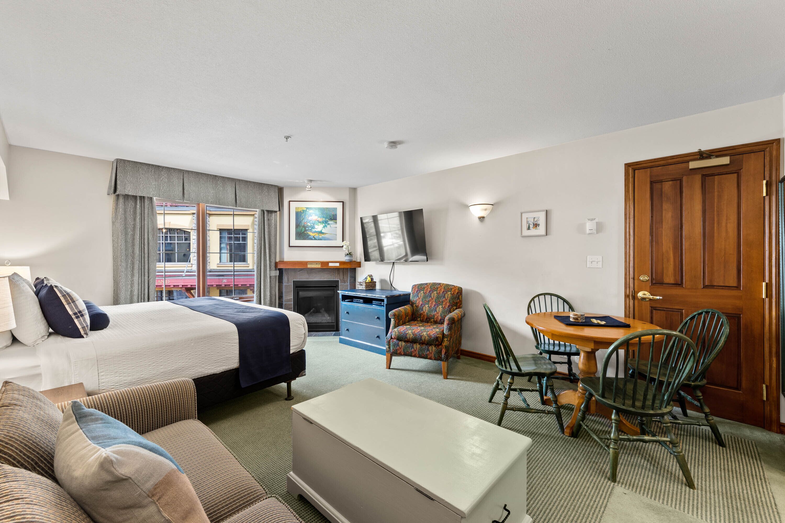 A hotel room with a bed, a sofa, a dining table with chairs, a television, and a fireplace.