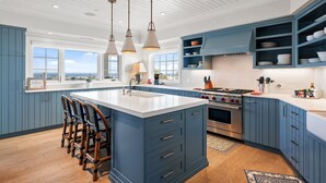 Una cocina con armarios azules, una isla grande con taburetes de bar, una estufa y vistas por las ventanas.