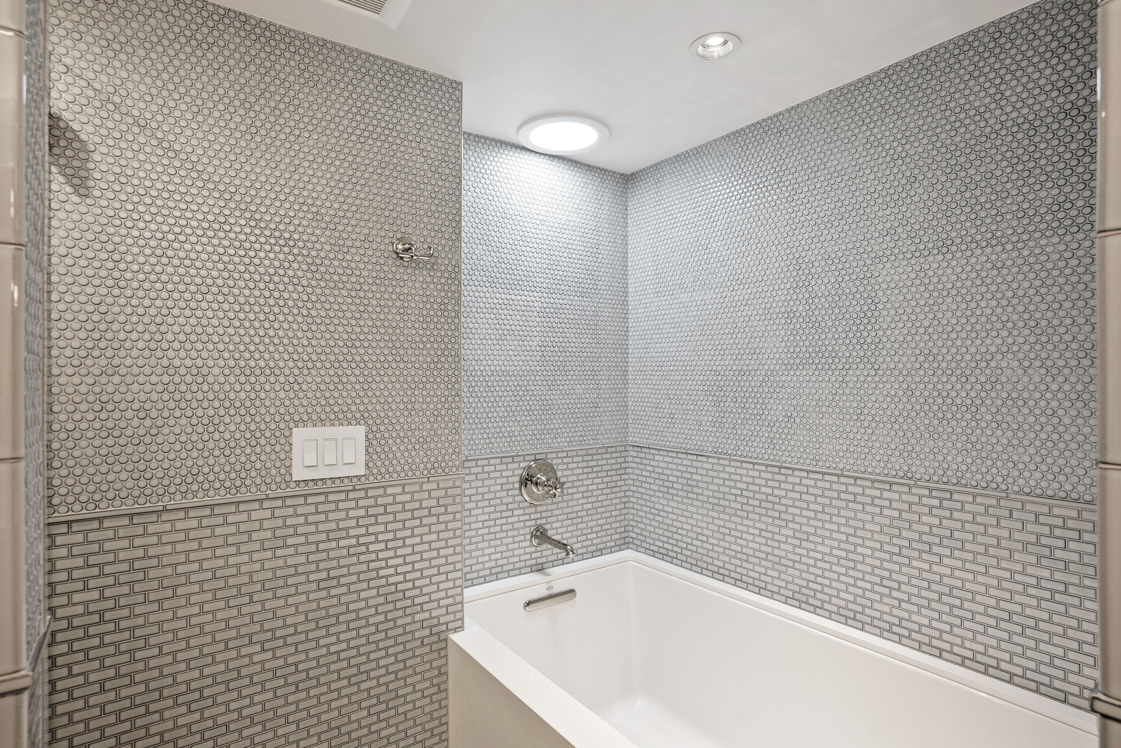 Een badkamer met een witte badkuip, betegelde muren en een plafondlamp.