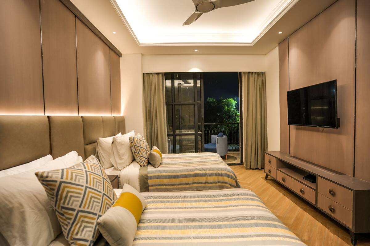 A modern bedroom with two beds, a TV, and a balcony with curtains.