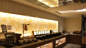 A well-lit buffet area with a marble backsplash, a coffee machine, and various food items displayed on shelves. - Atithi House (Greater Noida)