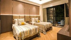 A hotel room with two beds, a ceiling fan, and a large window with a view of greenery. - Atithi House (Greater Noida)