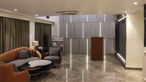 A modern hotel lobby with a sofa, armchairs, a coffee table, a reception desk, and a magazine rack. - Atithi House (Greater Noida)