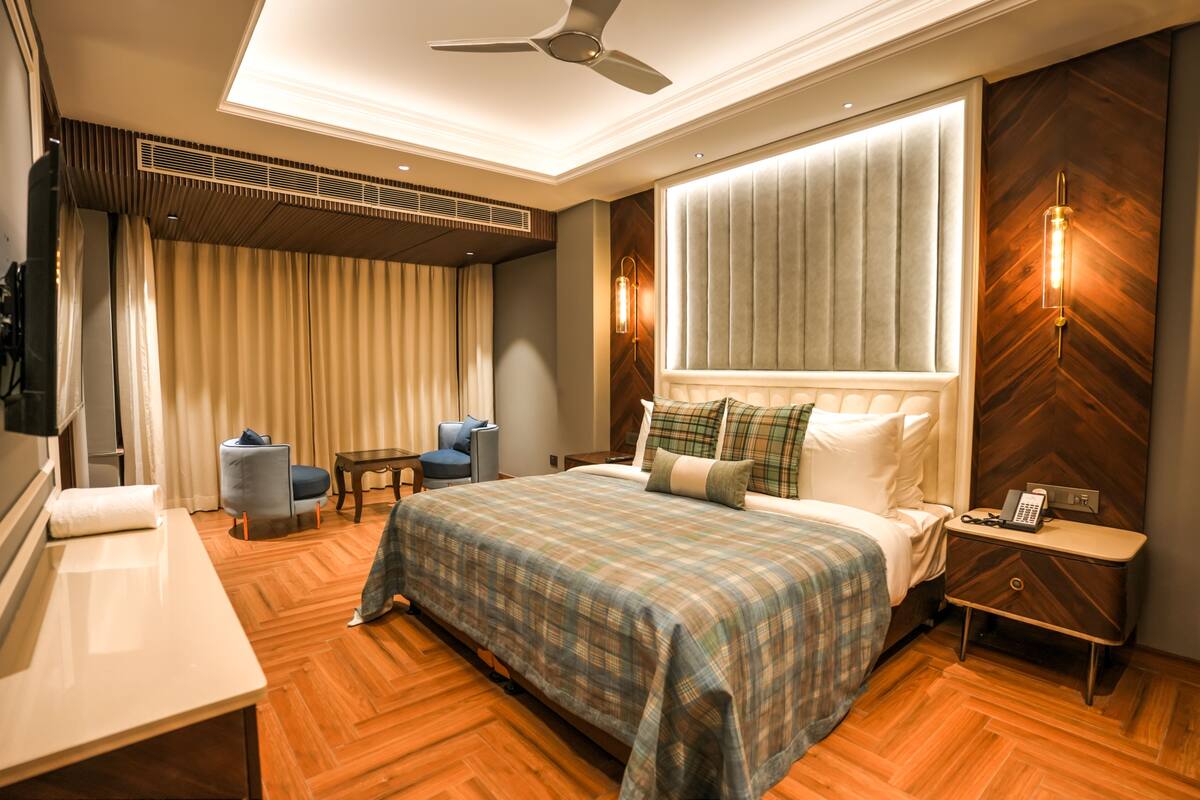 A hotel room with a large bed, a desk, a chair, a vanity, and a ceiling fan.