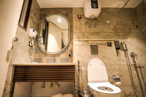 A bathroom with a marble floor, a round mirror, a toilet, a sink, and a handheld showerhead. - Atithi House (Greater Noida)