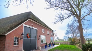 A brick building with a large garage door, a small window, and a door with a wreath. There are potted plants and a statue on the ground. - Garden View (Double or Twin) (Overschild)